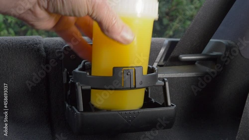 Closeup POV shot of a man's hand opening a foldaway cupholder in a vehicle, then placing a plastic container with a cold orange juice drink inside. photo