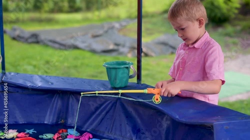 Little boy fisher catching plastic toy fish on pool amusement park summer day. Little boy have fun on fishing. Happy childhood.