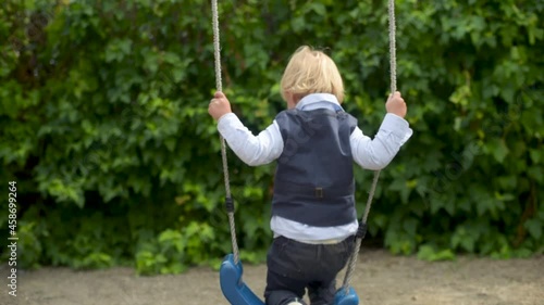 Child playing with swing outdoor. Adorable cute baby infant boy child at playground swinging. Portrait of happy child, rest in park, kid having fun playing in fresh air.