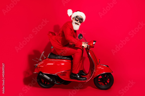 Photo of cute impressed age gentleman wear new year costume spectacles riding motorcycle smiling isolated red color background