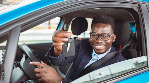 Portrait Of Young Happy Man Showing The Key Sitting In New Car. Young happy African American man sitting in a car and showing his car key while looking at camera.