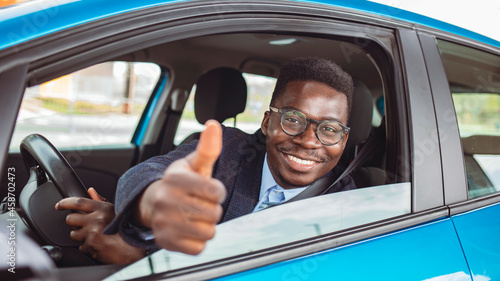 Man in a car with thumbs up. Happy smiling man sitting inside car showing thumbs up. Handsome guy excited about his new vehicle. Positive face expression.