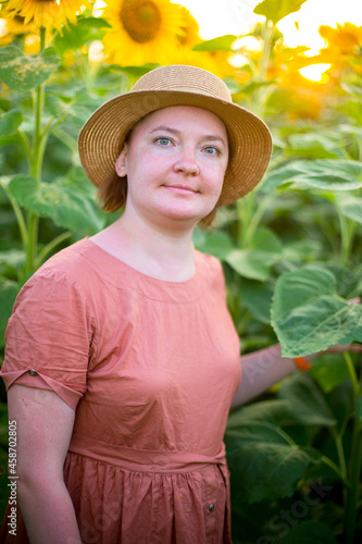 fat racy girl in a hat and dress is in the sunflowers in soft sunlight