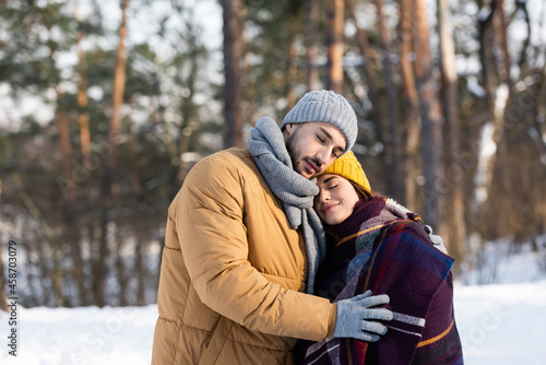 Young couple in warm clothes and blanket hugging in winter park