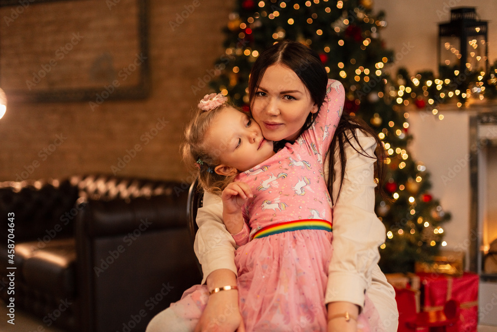 Beautiful happy mother with her daughter in fashionable clothes near the Christmas tree and lights. Family winter holidays
