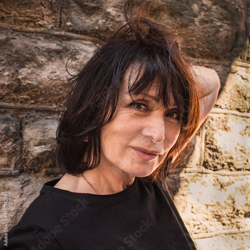 Portrait of a 65 year old brunette woman against a  old wall background.Close-up image, warm tone.