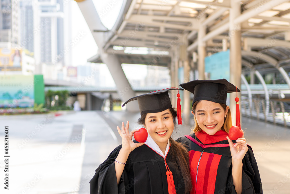 Two women in graduation gowns holding two red hearts.