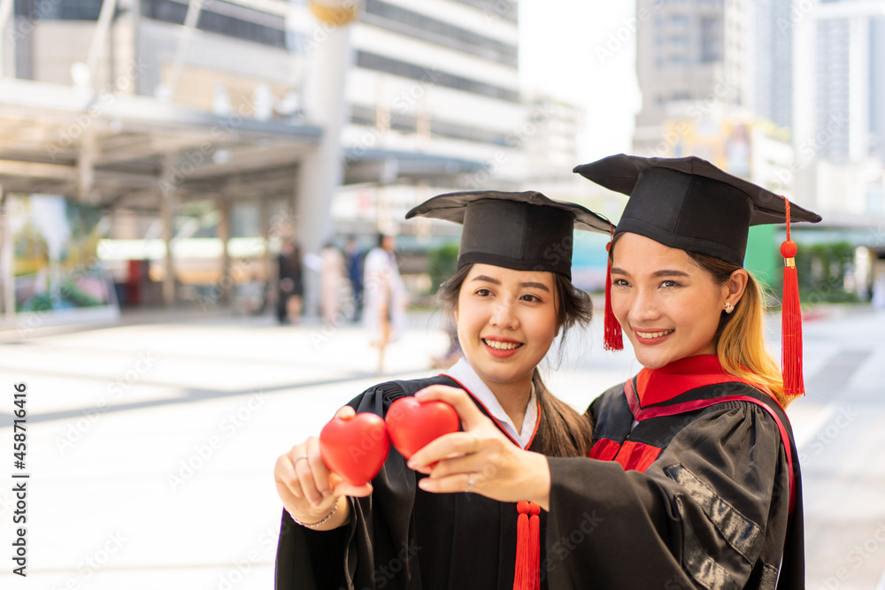 Two women in graduation gowns holding two red hearts.