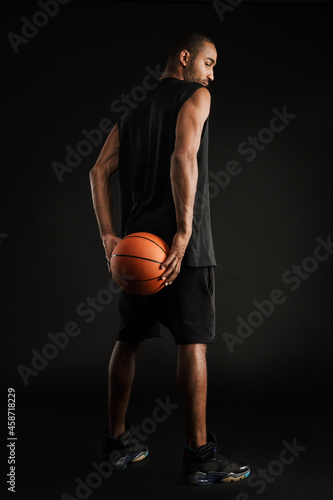 Young sportsman looking downward while posing with basketball
