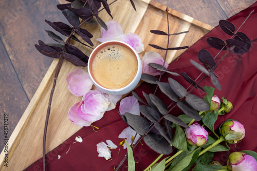 A white Cup of black coffee stands on a wooden background next to pink peonies and other garden flowers and leaves, The concept of village life, Cottagecore, ruralcore, cluttercore. High quality photo photo