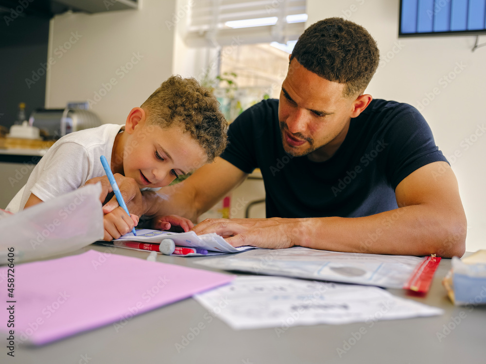 Father assisting son doing homework at home Father assisting son doing homework at home