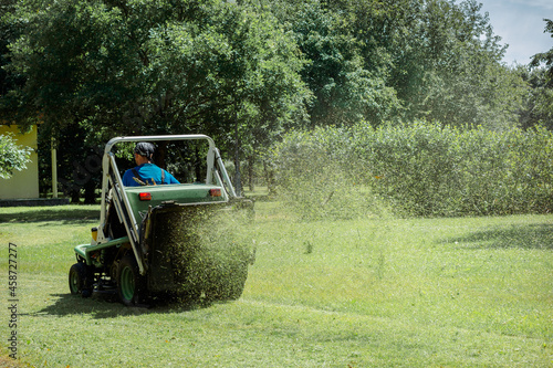 Professional gardener cutting green grass on lawn mower machine in park photo