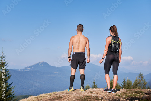 Rear view of sporty man and woman standing on top of rock and admiring beautiful scenery of mountain beskids. Hiking in the mountains. Concept of sport  travelling and nature.