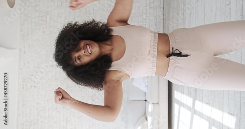 Trendy happy black mixed race woman vlogger listeng music, dances and recording videostream video for social media at home. Creating dancing video using tiktok app. Vertical video. photo