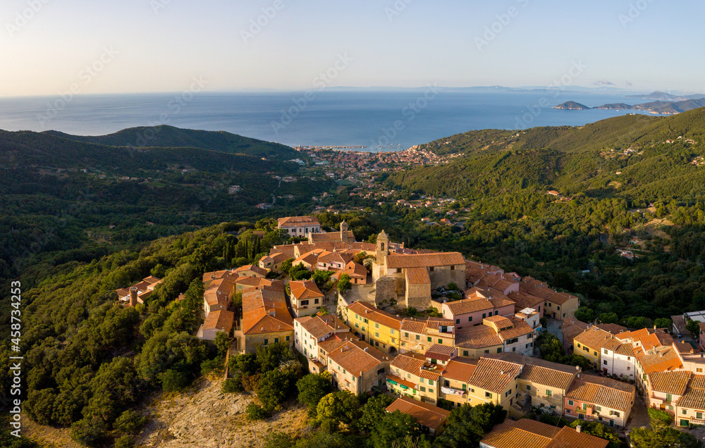 Obraz premium Aerial Drone Panorama of mountain old town Marciana on the islands of Elba Italy with green trees and the mediterranean sea ocean in the background