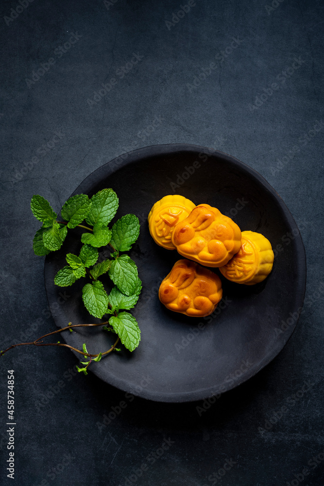 The mooncakes on a plate isolated on dark gray background. Traditional Chinese Pastry, mid-autumn Moon cake, souffle. The mooncakes on a plate isolated on dark gray background. Traditional Chinese Pastry, mid-autumn Moon cake, souffle.