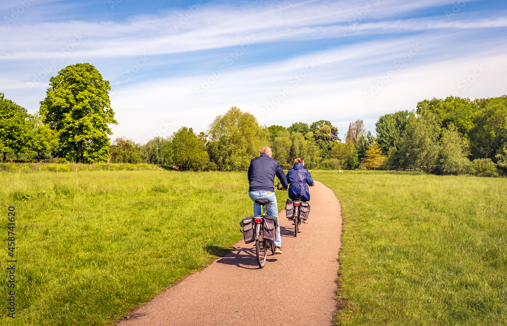 Obraz premium A man and a woman are cycling on a curved bicycle path in a Dutch nature reserve. It is a sunny day in the spring season.