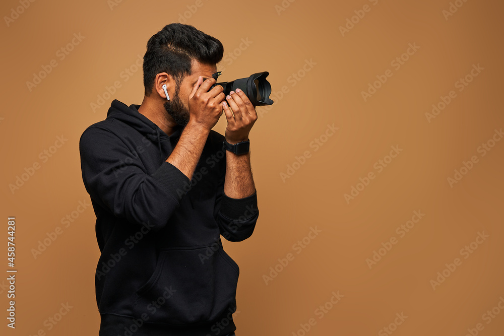 Young indian videographer in black hoody with camera on background with copy space Young indian videographer in black hoody with camera on background with copy space