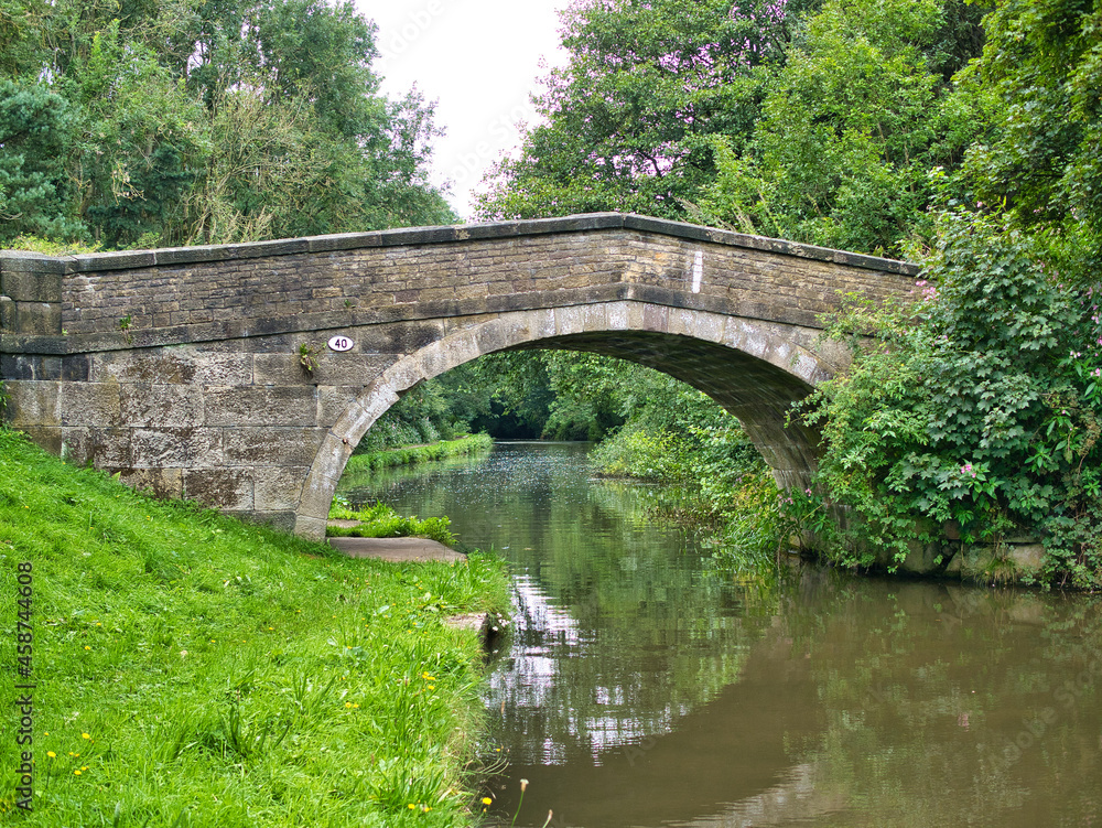 An old stone bridge reflected in the water of the Leeds Liverpool Canal in a rural setting on the in Lancashire, UK. An old stone bridge reflected in the water of the Leeds Liverpool Canal in a rural setting on the in Lancashire, UK.