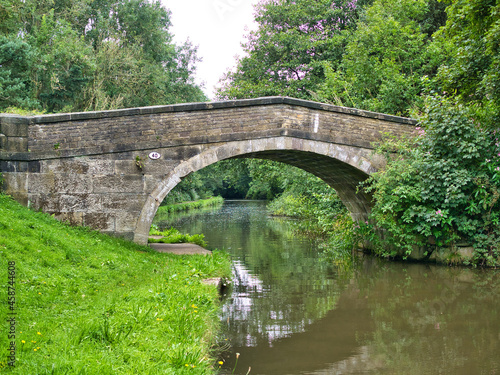 An old stone bridge reflected in the water of the Leeds Liverpool Canal in a rural setting on the in Lancashire, UK.