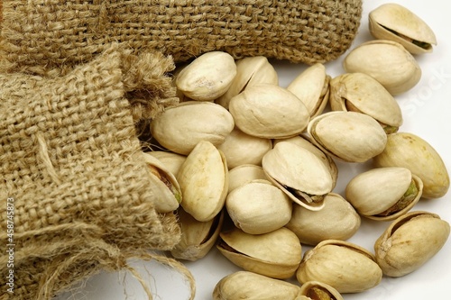 Small sacks of burlap filled with rousted pistachios seeds with shell lie on a white table. photo