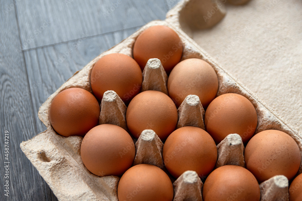 Brown hen eggs lie in a row in a box made of recycled cardboard are located on a grey wooden surface. Healthy farm food