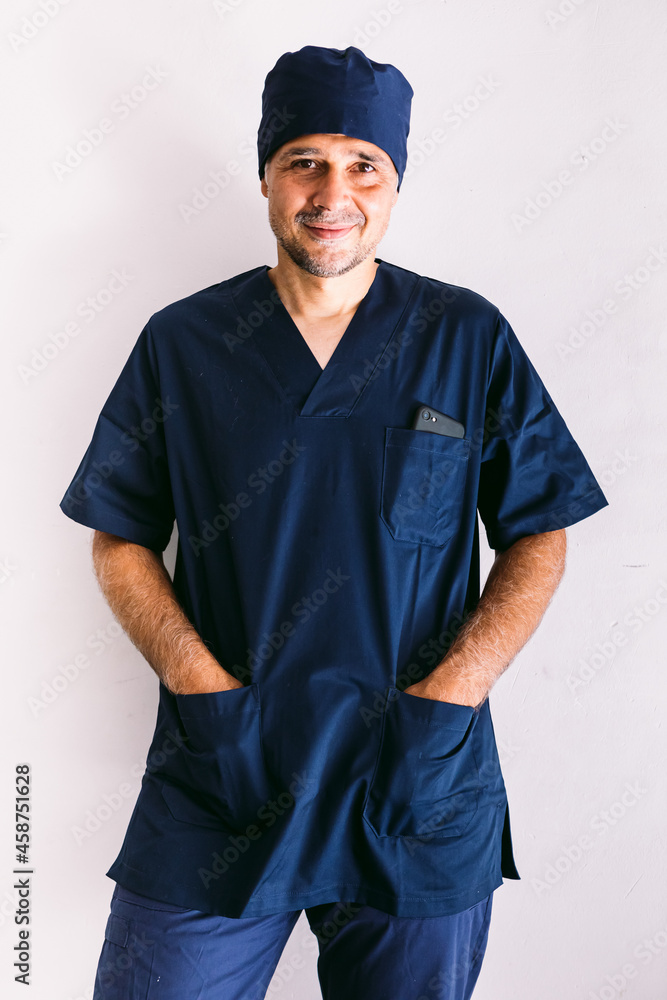 Male nurse, doctor or vet in blue uniform at a window in a hospital, hands in pockets, smiling. Medicine, hospital and healthcare concept. Male nurse, doctor or vet in blue uniform at a window in a hospital, hands in pockets, smiling. Medicine, hospital and healthcare concept.