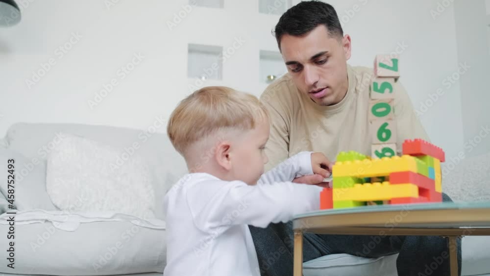A positive father playing with his son holding a constructor sitting on the couch A positive father playing with his son holding a constructor sitting on the couch