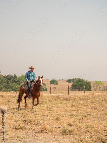 Cowboy is riding his horse on a cattle farm with very dry land