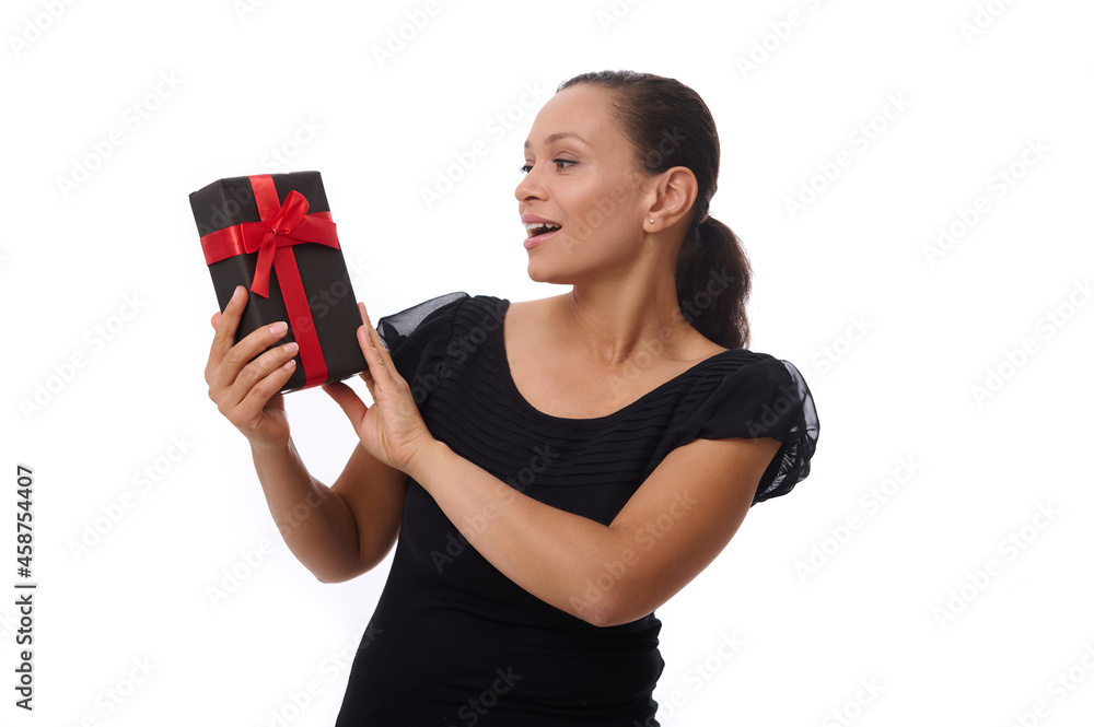 Beautiful happy Latin American woman dressed in black outfit poses against a white background , smiles toothy smile looking at a black gift box in her hands. Black Friday concept copy space for ad Beautiful happy Latin American woman dressed in black outfit poses against a white background , smiles toothy smile looking at a black gift box in her hands. Black Friday concept copy space for ad