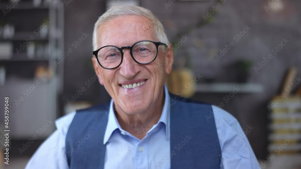 Portrait closeup of a happy self-confident attractive old executive businessman with black modern glasses looks at camera and smiles at the office or at home. Portrait closeup of a happy self-confident attractive old executive businessman with black modern glasses looks at camera and smiles at the office or at home.
