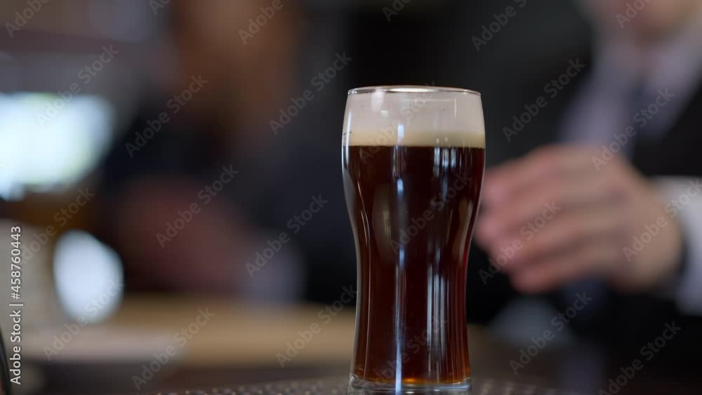 Close-up beer glasses on bar counter with male hand taking pale and dark lager blurred men clinking toasting at background. Unrecognizable Caucasian and African American colleagues resting after work Close-up beer glasses on bar counter with male hand taking pale and dark lager blurred men clinking toasting at background. Unrecognizable Caucasian and African American colleagues resting after work