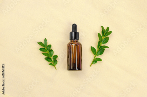 An essential oil or serum made from natural ingredients. Cosmetic bottle with dropper on bamboo fabric with green leaves. Eco-friendly cosmetics.