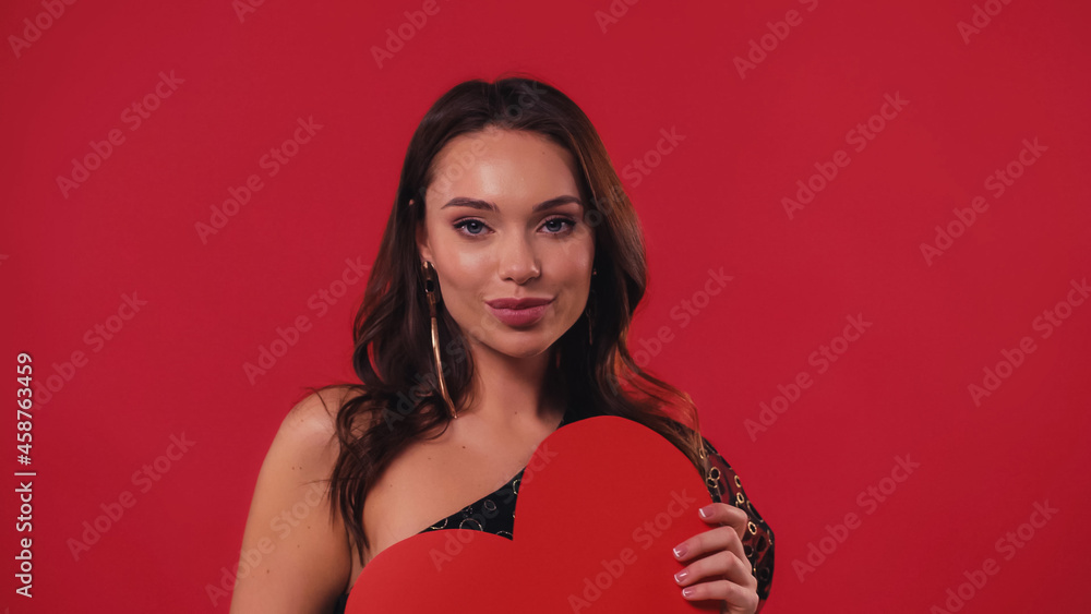 young and pleased woman holding paper heart isolated on red. young and pleased woman holding paper heart isolated on red.