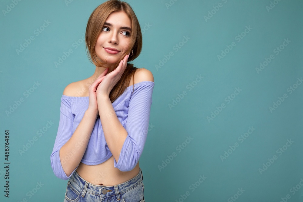 Young cute happy beautiful dark blonde woman with sincere emotions isolated on background wall with copy space wearing casual blue crop top. Positive concept Young cute happy beautiful dark blonde woman with sincere emotions isolated on background wall with copy space wearing casual blue crop top. Positive concept