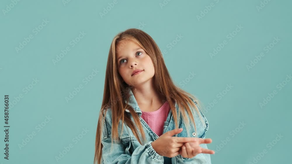 A serious small girl wearing jeans jacket counting on fingers standing isolated over a blue wall in the studio A serious small girl wearing jeans jacket counting on fingers standing isolated over a blue wall in the studio