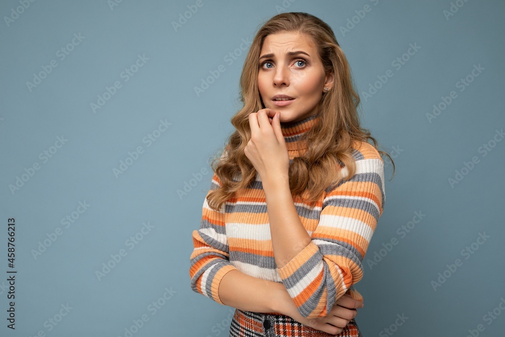 Photo shot portrait of young nice winsome beautiful sad upset thoughtful blonde woman with sincere emotions wearing striped sweater isolated over blue background with free space and having problems Photo shot portrait of young nice winsome beautiful sad upset thoughtful blonde woman with sincere emotions wearing striped sweater isolated over blue background with free space and having problems