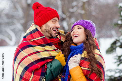 Photo of adorable funny girlfriend boyfriend dressed vests covering plaid duvet laughing embracing walking snow outdoors forest © deagreez