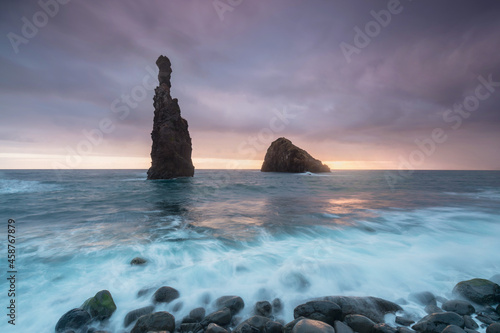 Morning seascape sunrise of Madeira. Rocky shore, silhouette of two steep cliffs and misty rocks hit by waves. Long exposure. Ribeira da Janela, traveling Madeira island, Portugal. Volcanic rocks