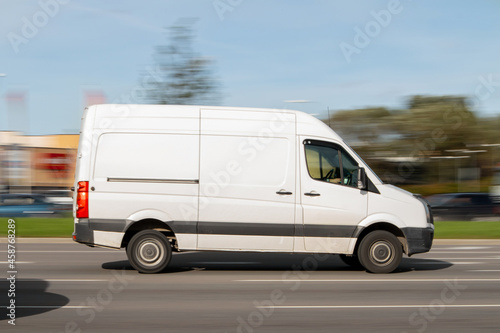 A white van drives fast down the street. Commercial vehicles for small loads, parcel deliveries. Motion blur