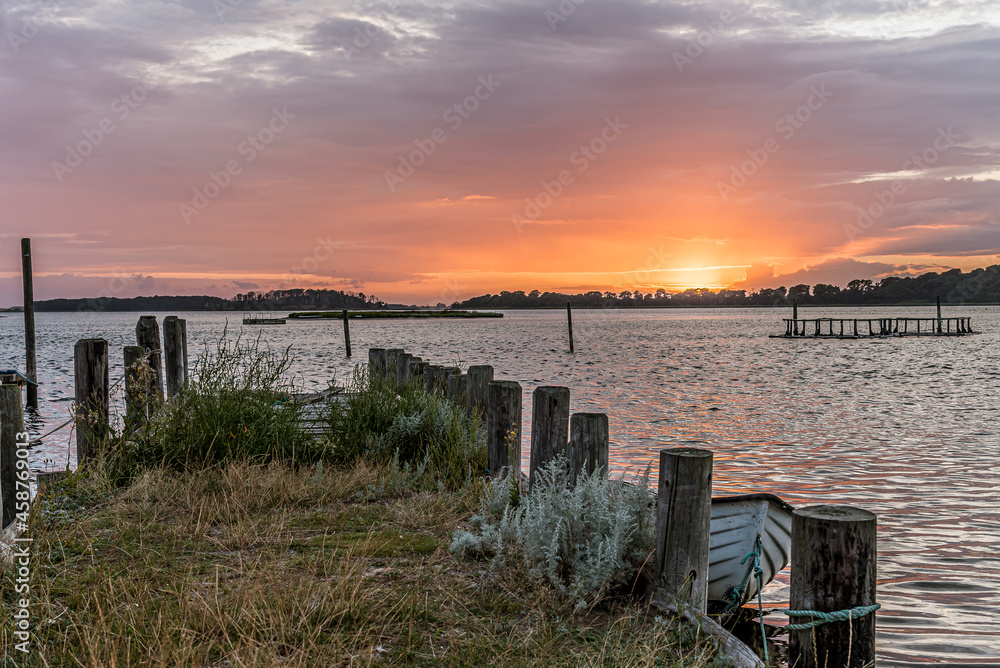 a moored rowing boat at a jetty of old piles in the sunset