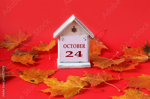 Calendar for October 24 : decorative house with the name of the month in English, the number 24, autumn maple leaves on a red background, side view