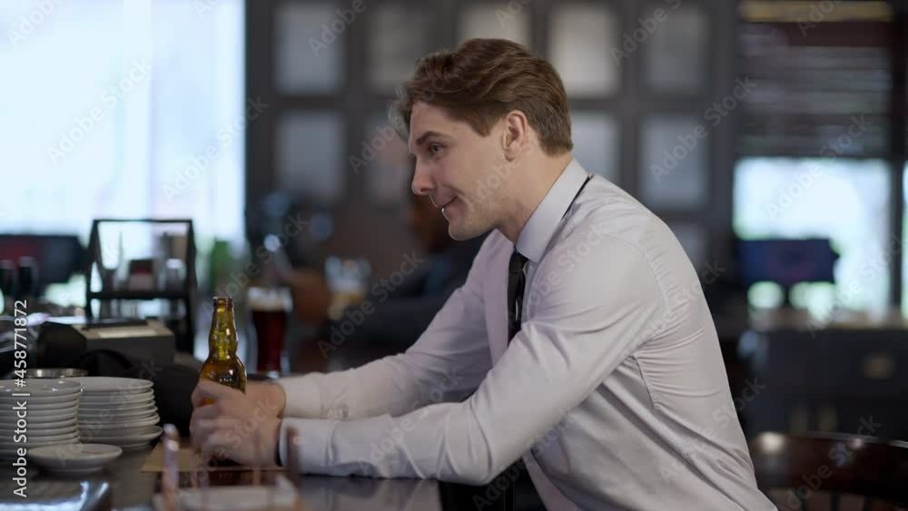 Side view of relaxed businessman drinking beer ordering more alcohol at bar counter. Portrait of successful young handsome Caucasian man enjoying Friday. Blurred African American guy at background Side view of relaxed businessman drinking beer ordering more alcohol at bar counter. Portrait of successful young handsome Caucasian man enjoying Friday. Blurred African American guy at background