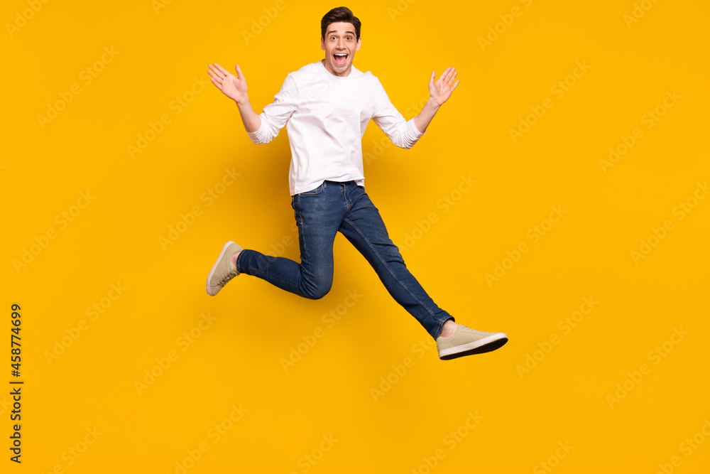 Full size photo of funny brunet millennial guy jump wear shirt jeans sneakers isolated on yellow background