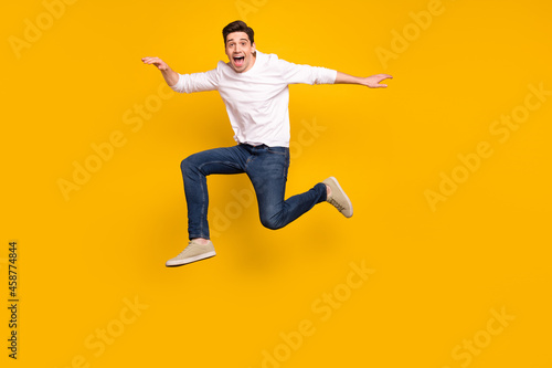 Full body photo of cool brunet young guy jump wear shirt jeans sneakers isolated on yellow background © deagreez