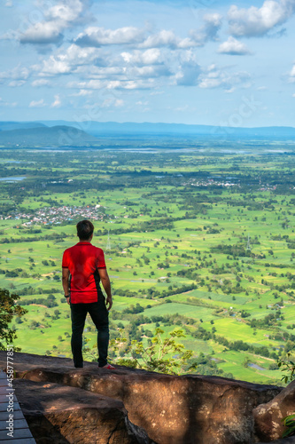 Working Young man standing on top of cliff in summer mountains at enjoying view of nature, at Pha Chom Tawan in Phu Wiang National Park, Khon Kaen, Thailand.