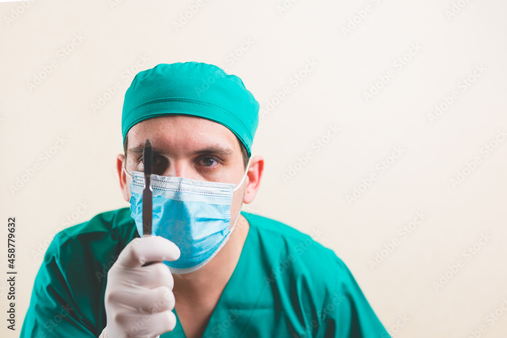 Focused doctor in green surgeon suit and protective breathing mask with lancet on the yellow background isolated Focused doctor in green surgeon suit and protective breathing mask with lancet on the yellow background isolated