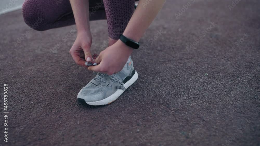 Sports woman kneeling down to tie shoelaces on her sneakers, slow-motion Sports woman kneeling down to tie shoelaces on her sneakers, slow-motion
