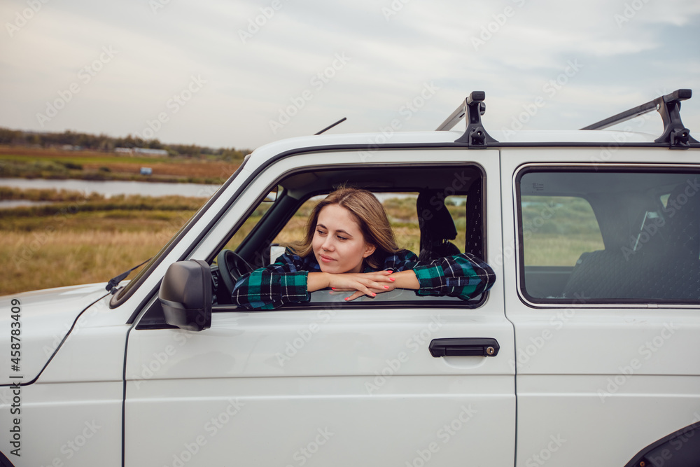 A young woman looks out of the window of an SUV and admires the nature.