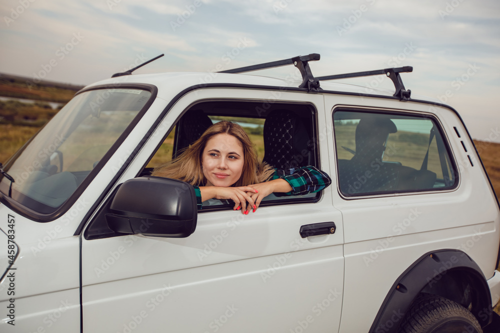 A young woman looks out of the window of an SUV and admires the nature. A young woman looks out of the window of an SUV and admires the nature.